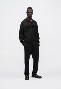 Fekete pulóver és nadrág "HUGO" logóval azonos színben. Minimalista kialakítás, lágy textúrával és kényelmes szabással. A fekete cipő teszi teljessé a megjelenést.