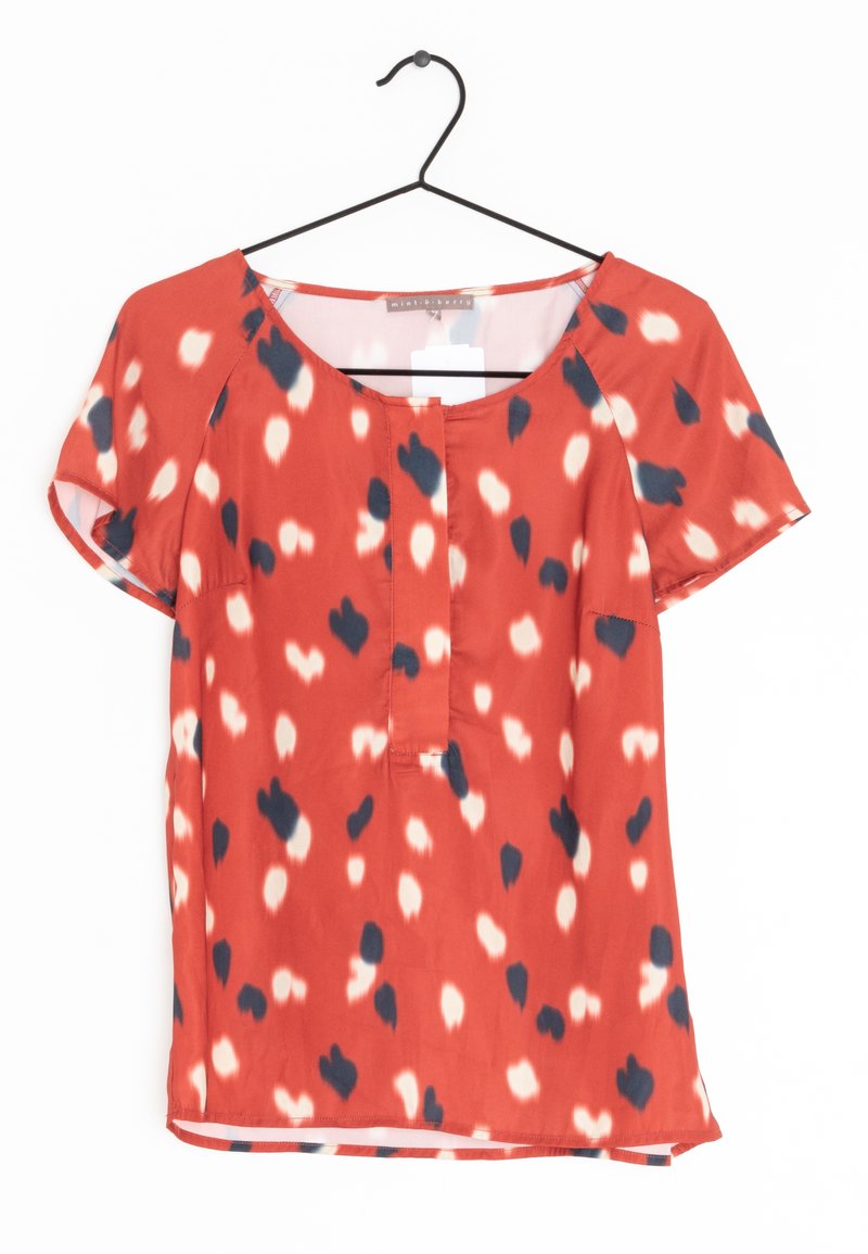 Red blouse made of smooth fabric, featuring a round neckline, short sleeves, and a front placket with black and cream abstract spots.