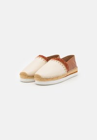 Par slip-on espadrille-sko med cremefarvet forside, brun læderbagside, vævet kant og hvide gummisåler på hvid baggrund.