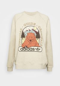 Beige sweatshirt med rund hals, med en illustration av en björn, berg och texten "Official Guide Originals" ovanför adidas-logotypen.