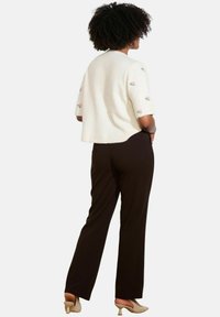 Maglione bianco corto a maglia con ricamo di fiori rosa sulle maniche, abbinato a pantaloni neri a gamba dritta e tacchi beige.