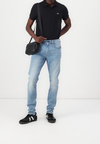 Svart polo skjorta, ljusblå jeans, svarta sneakers med vita ränder, och en liten svart crossbody-väska. Klassisk passform, avslappnad design.
