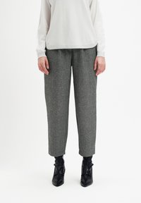 Osoba ubrana w szare spodnie w jodełkę, białą bluzkę z długim rękawem oraz czarne botki za kostkę stoi na białym tle.