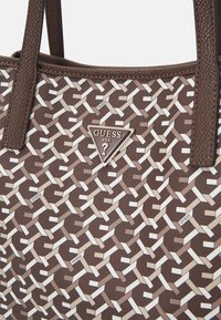Sac fourre-tout à motif marron en matériau synthétique, doté d'une plaque-logo triangulaire et d'un design tissé dans des teintes crème et beige.