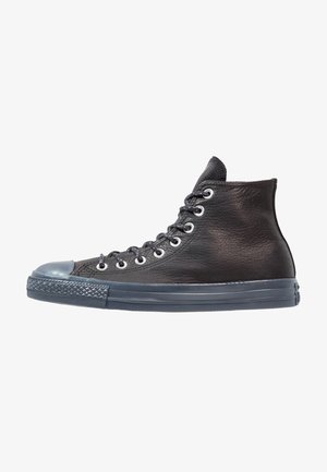 Czarny skórzany sneaker typu high-top z szarą gumową podeszwą, szarą nakładką na palce i czarnymi sznurówkami przewleczonymi przez metalowe oczka.