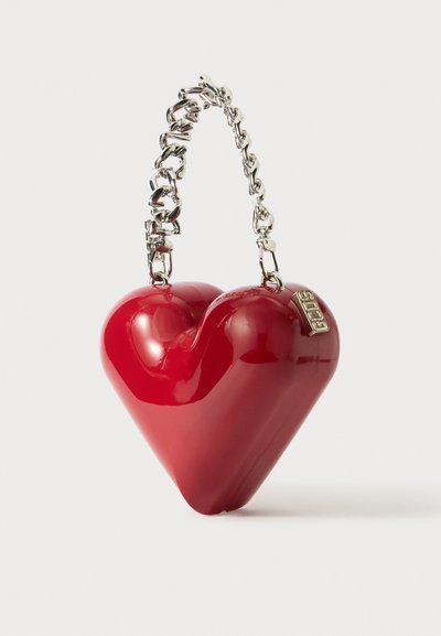 Czerwona torebka w kształcie serca, wykonana z błyszczącego materiału, z metalicznym srebrnym łańcuszkiem i małym tagiem marki.