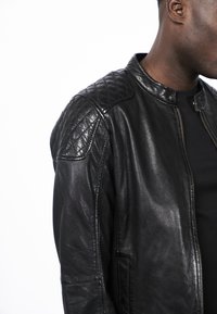 Černá kožená bunda s předním zipem, prošívanými ramenními okraji a hladkým povrchem. Má stojatý límec a boční kapsy.