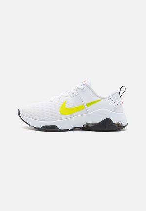 Biało-czarny but sportowy z żółtym logo Nike, cholewką z siateczki, amortyzowaną podeszwą i pętelką na pięcie, widoczny z zewnętrznego profilu bocznego.