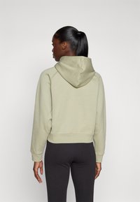 Moleton cropped verde claro com capuz ajustável, mangas raglan e punhos canelados, combinado com leggings pretas. Textura suave.