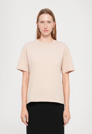Lys beige kortermet t-skjorte laget av mykt stoff med rund hals og avslappet passform, brukt over et svart skjørt.