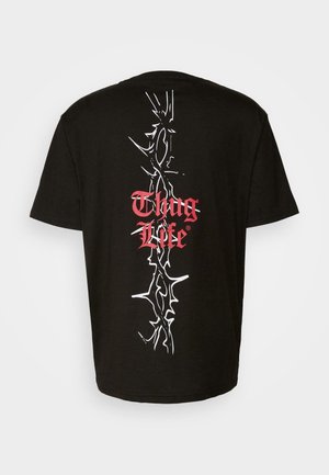 Schwarzes Baumwoll-T-Shirt mit weißem, dornenartigem Grafikdesign und rotem "Thug Life"-Text, der zentriert auf dem Rücken aufgedruckt ist. Kurze Ärmel, normale Passform.