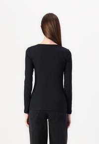 Zwart langemouwtop gemaakt van ribstof met een ronde hals, aansluitend ontwerp en een gladde textuur. Gecombineerd met donkere broek.