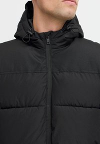 Schwarze Daunenjacke mit Reißverschluss und verstellbarem Kapuzen. Sie zeichnet sich durch ein gestepptes Muster und eine glatte Textur aus, die für kaltes Wetter geeignet ist.