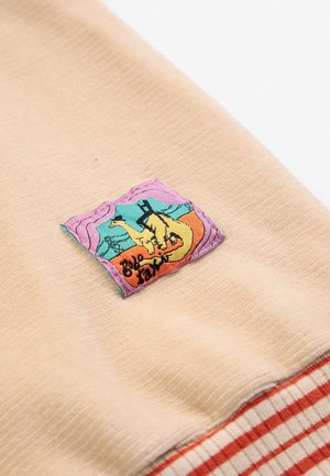 Beige stof met een kleurrijke gestikte patch waarop een kameel met een zwarte hoed en een man die achterstevoren op hem zit, te zien is.