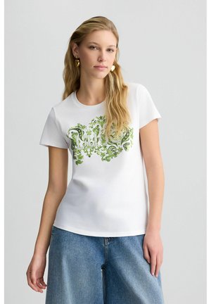 T-shirt bianco in cotone con motivo floreale verde e testo stilizzato. Maniche corte, scollo rotondo e una vestibilità rilassata.