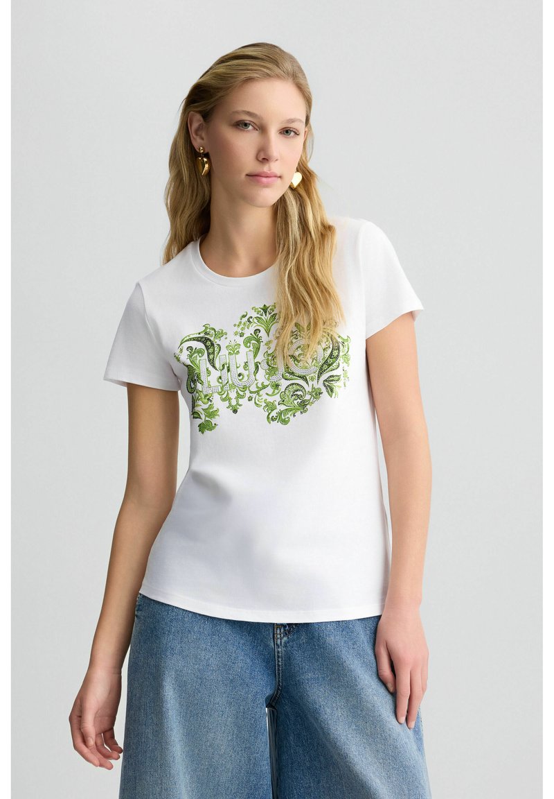 T-shirt en coton blanc avec un design de fleurs vertes et un texte stylisé. Manches courtes, col rond et coupe décontractée.