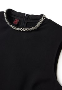 Vestido negro sin mangas con un cuello alto adornado con un collar de rhinestones plateados y cierre de cremallera en la parte posterior. Textura de tela suave.