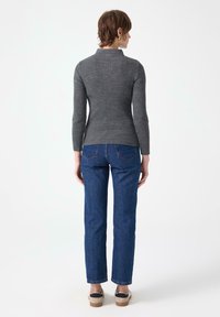 Hall griimude ribidega pikkade varrukatega topp, mis on paaritatud siniste sirgete säärega teksapükstega. Topp sisaldab kõrget kraed, samas kui teksapükstel on dekoratiivsed tagataskud.