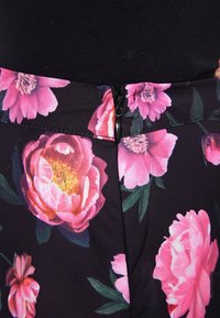 Jupe florale ornée de grandes pivoine roses sur un fond sombre, avec une fermeture éclair discrète à l'arrière. Texture de tissu lisse.