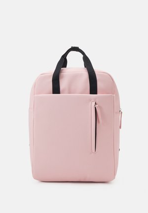 Sac à dos carré rose pâle avec poignées noires et poche zippée verticale à l'avant sur fond blanc.