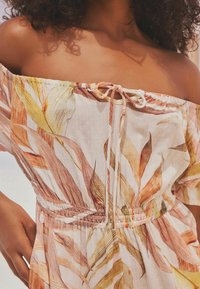 Robe décolletée en tissu léger, dotée d'un motif floral dans des tons d'orange doux et de vert, avec une taille élastique et un détail de cordon.