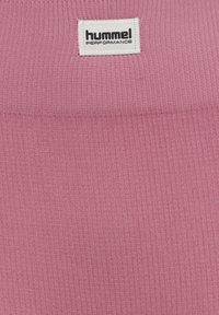 Roze ribstof met een wit etiket waarop "hummel PERFORMANCE" staat. De textuur is glad en gelijkmatig door het hele ontwerp.