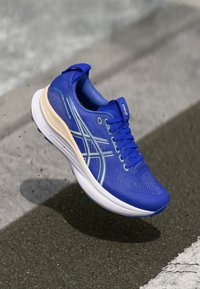 Blauer Laufschuh mit einem strukturierten Mesh-Obermaterial, Kunststoffakzenten, reflektierenden Details, einer gepolsterten Sohle und einer leicht verjüngten Form.