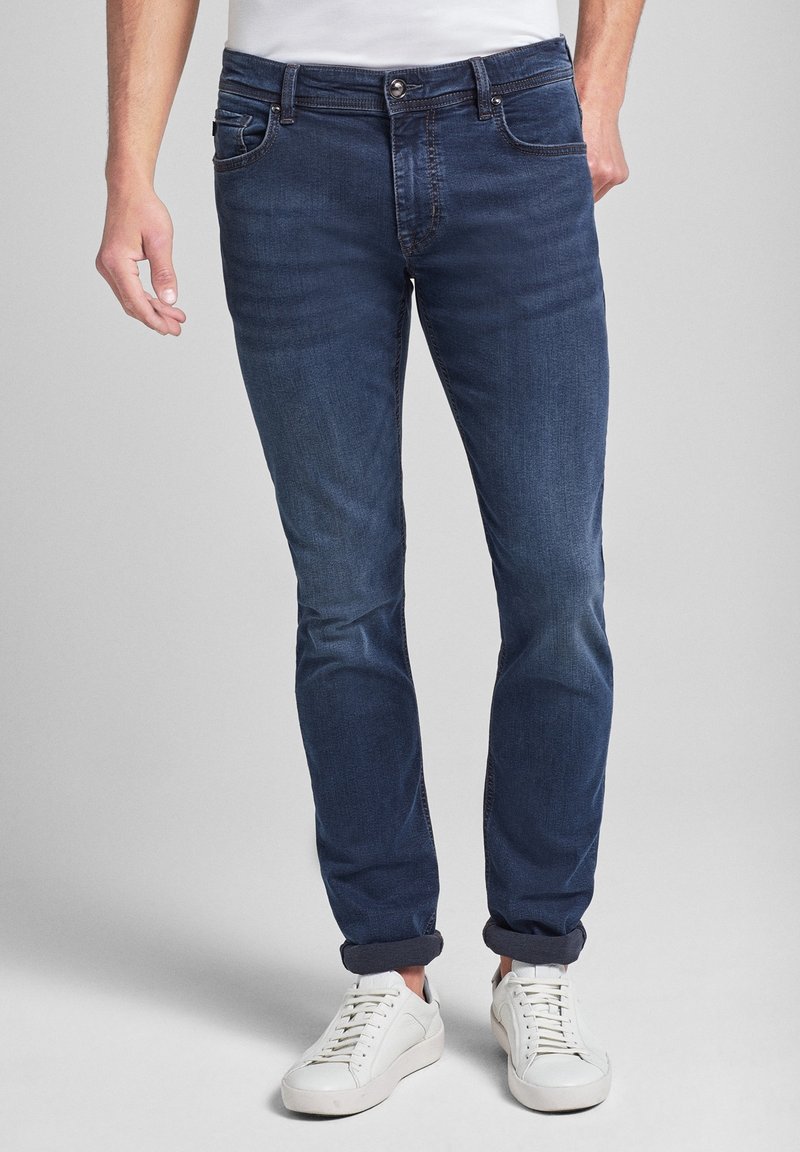 Mörkblå denimjeans med slim fit, fem fickor, diskret sömnad och uppvikta benslut, kombinerat med vita sneakers.