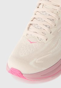 Lys rosa joggesko med en teksturert overdel, flate lisser og en rosa gummisåle. Har ventilasjonsåpninger og et karakteristisk logodesign.