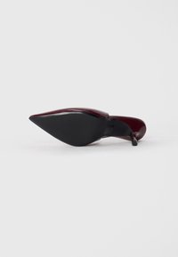 Escarpin en cuir verni bordeaux avec un bout pointu et un talon fin. La semelle est dotée de caoutchouc noir texturé pour une meilleure adhérence.