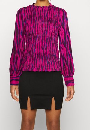 Woman wearing a long-sleeve pink and black patterned blouse and a black mini skirt with two front slits.