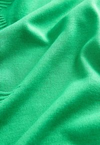 Vihreä neulottu kangas, jossa on sileä rakenne, jossa on joustava kudonta ja hienovaraisia sävyvaihteluita pinnan läpi.