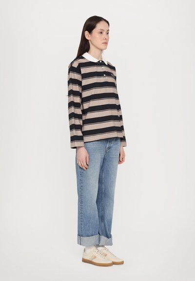 Striped langermet polo i beige og svart, med en hvit krage. Kombinert med lyseblå denimjeans og nøytrale sneakers.