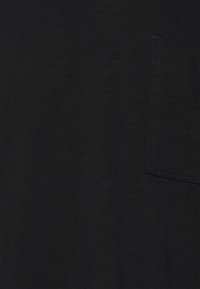Tessuto nero strutturato con una piccola tasca cucita sul lato destro, che mostra dettagliate linee di cucitura e una sottile trama del tessuto.