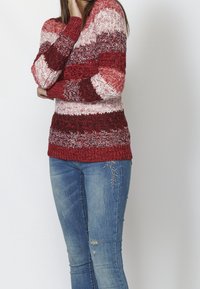 Sweter z dzianiny w czerwone, białe i burgundowe paski; teksturowana tkanina; ściągacze przy mankietach i u dołu; noszony z podartymi niebieskimi dżinsami z haftem.
