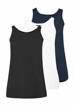 Femme debout portant un débardeur blanc, un jean skinny bleu foncé et des baskets blanches sur un fond blanc uni.