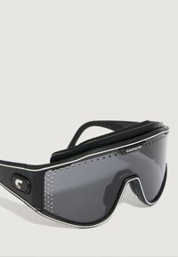 Occhiali da sole sportivi neri con design curvo, lenti scure, prese d'aria laterali e imbottitura in schiuma testurizzata lungo la parte superiore. Accenti argento vicino alle lenti.