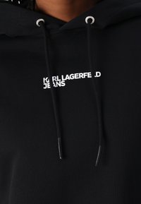 Black hoodie made of cotton, featuring a front logo in white text "KARL LAGERFELD JEANS," with silver eyelets and black drawstrings.