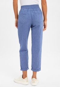 Light blue, woven fabric pants with an elastic waistband, rolled cuffs, and two back pockets, paired with white sneakers.