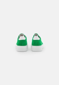 Chaussures en daim vert avec semelles en caoutchouc blanches ; bout rond et design texturé. La vue arrière montre un col rembourré et une doublure intérieure lisse.