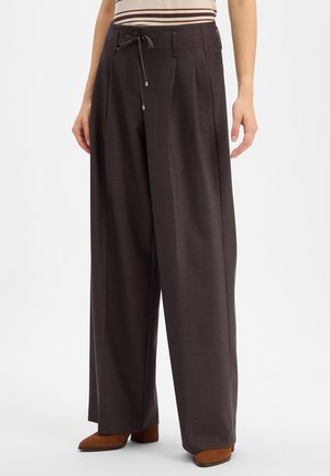 Losse donkerbruine wijde broek met plooien voor en een gestrikte tailleband, gedragen met bruine schoenen en een gestreept topje.