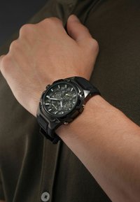 Orologio sportivo nero con cinturino in silicone testurizzato, cassa metallica rotonda e quadranti doppi che mostrano l'ora e la data su uno sfondo scuro.