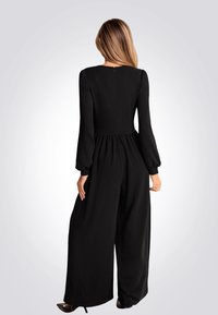 Combinaison noire avec des manches longues, un buste ajusté et un pantalon à jambes larges, dotée d'une fermeture éclair dans le dos et d'un détail de taille froncée.