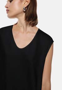 Top nero a maniche corte con scollatura a V profonda. Texture liscia e leggero lucido, accentuato da un design pulito e uno stile minimalista.