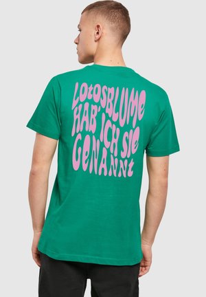 Grøn bomulds T-shirt med stor, bølget pink tekst på ryggen, der står "Lotosblume hab' ich sie genannt." Korte ærmer, rund hals.
