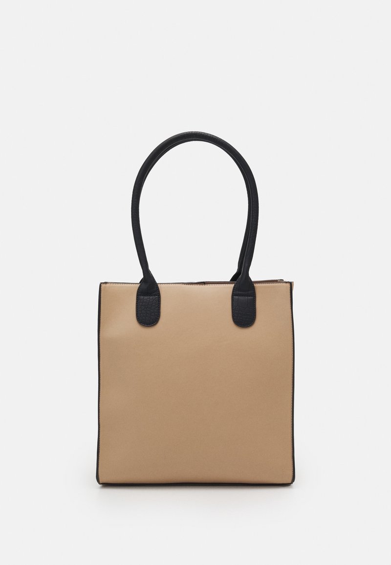 Sac à main carré beige avec de longues poignées noires et des points d'attache noirs texturés sur un fond uni.