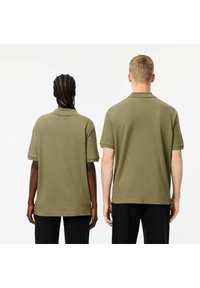 Olivgröna polo-tröjor i en avslappnad passform, korta ärmar och ribbade kragar. Tyget verkar slätt med en subtil textur, bärs av två personer.