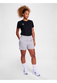 Tricou negru cu mânecă scurtă și logo alb, combinat cu pantaloni scurți de trening gri. Modelul purta adidași albi și șosete albe până la genunchi.