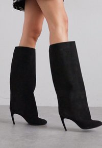 Melni zamšādas ceļgalu augstie zābaki ar smailu purngalu un stiletto papēdi, ar gludu tekstūru un pieguļošu siluetu.