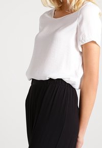 Vit kortärmad blus med lös passform och rundad halsringning, i kombination med svarta plisserade byxor med hög midja. Slät tygkänsla.